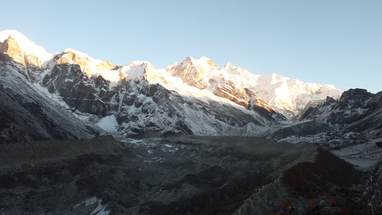 Golden sunrise illuminating snowy peaks of Machhapuchhre Mountain in Nepal, transitioning from early morning shadows to glowing Himalayan light over rugged alpine terrain