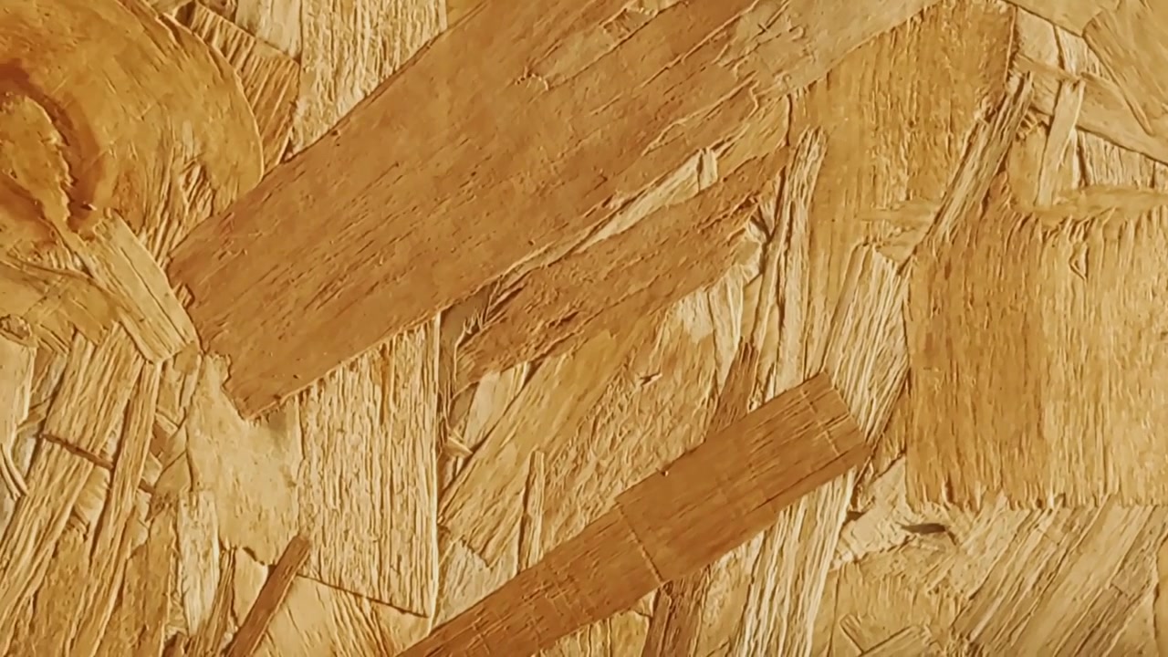 Detailní záběr na povrch OSB desky se stlačenými dřevěnými třískami, hrubou texturou, teplými žlutými tóny a detailem stavebního materiálu.