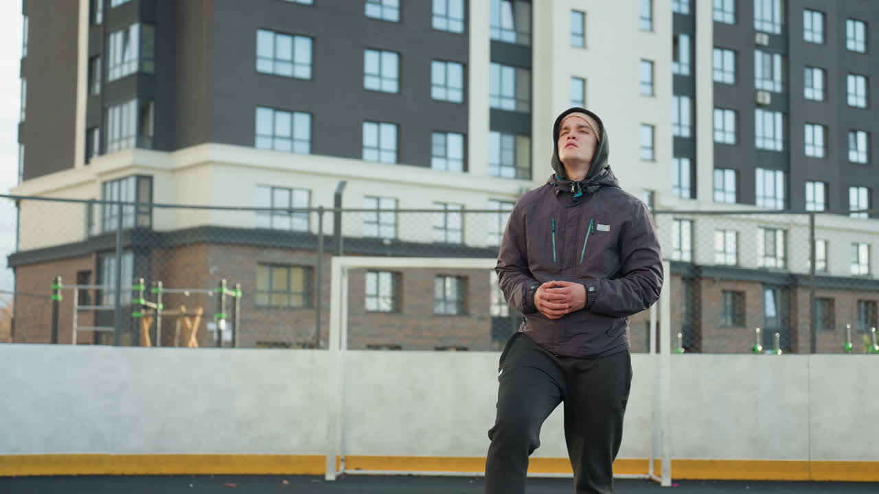Athlete turning head and stretching arms in preparation for sports activity in urban sports arena with modern residential buildings and goalpost in background