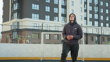 athlete turning head and stretching arms in preparation for sports activity in urban sports arena with modern residential buildings and goalpost in background