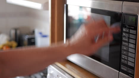 man places leftover meal in a white bowl into a microwave oven and sets the timer