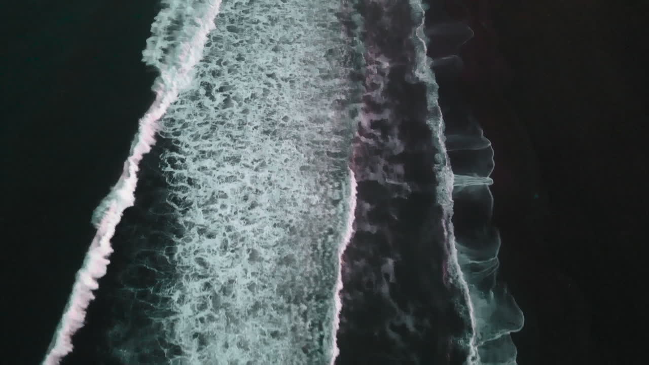 Aerial view of waves on a dark beach