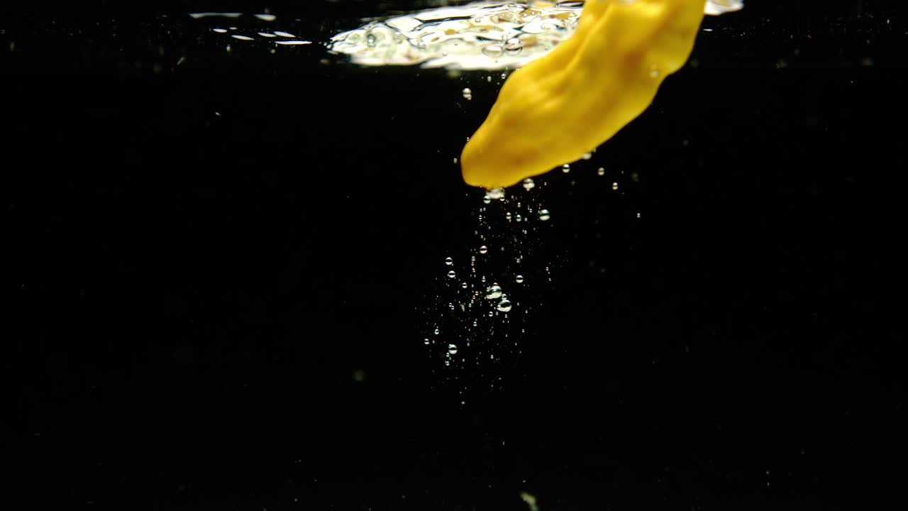 súper cámara lenta de fresca madame jeanette pimientos cayendo en el agua sobre fondo negro