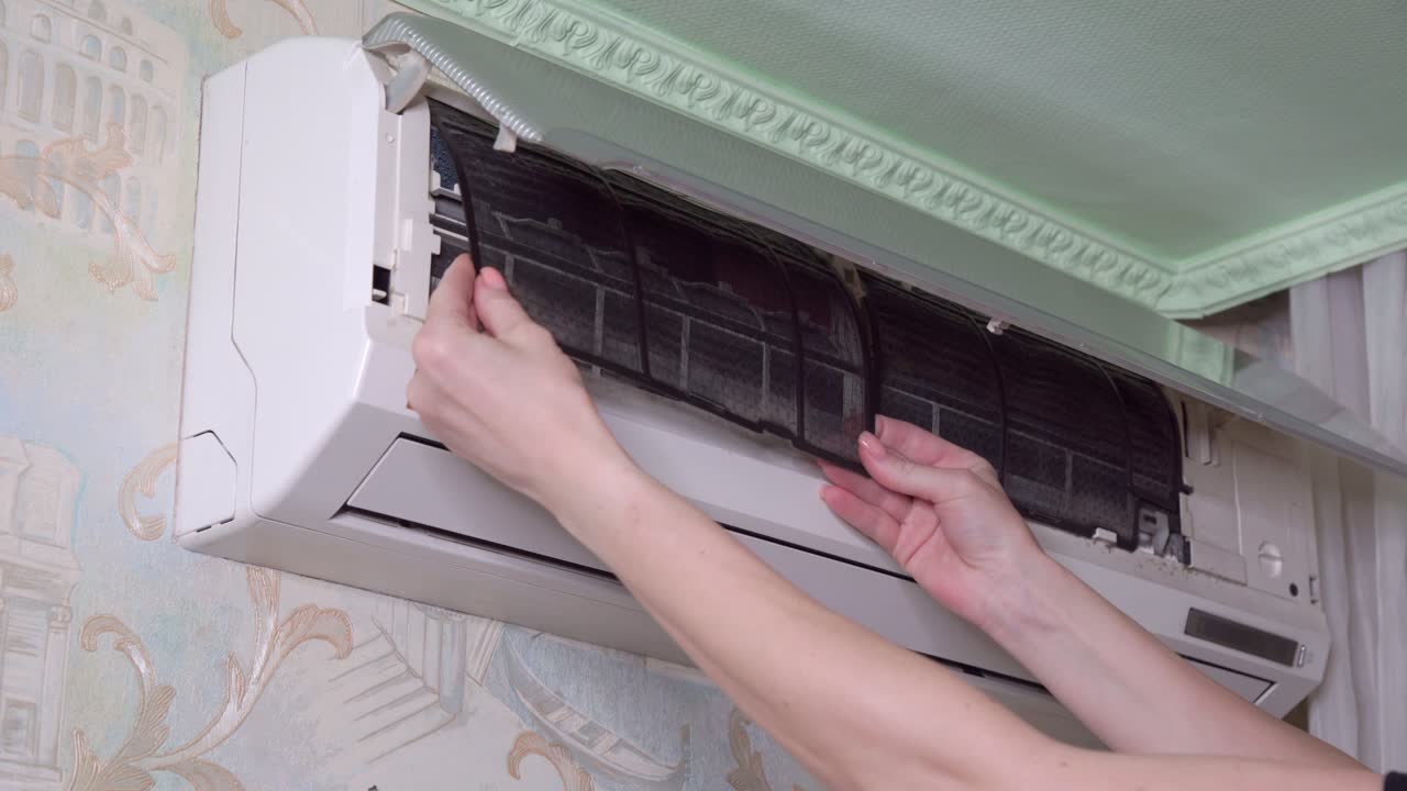 Women's hands remove dirty air filter from household air conditioner.