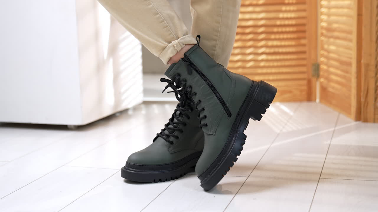 Grey elegant footwear with black laces and black tractor soles. Model in light jeans demonstrating stylish boots in studio.
