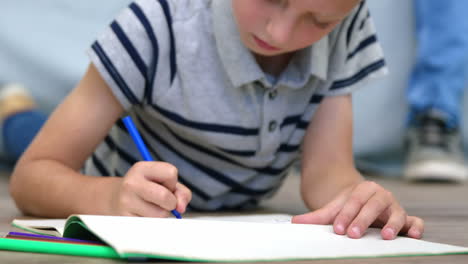 close up on a boy lying on a floor and doing colouring pictures