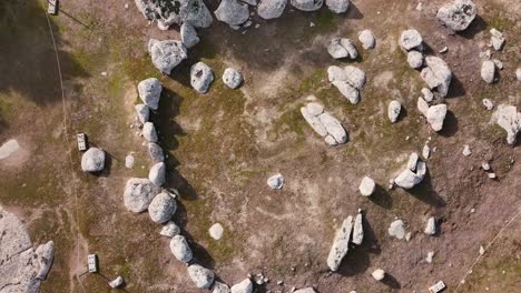 vuelo con un dron en ascenso con una vista de arriba hacia abajo y al mismo tiempo haciendo un giro visualizando un cromlech de piedra en un suelo marrón con una forma circular asegurada con una cuerda en toledo, españa
