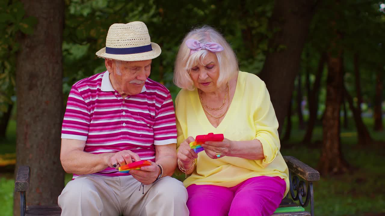 스타일리시한 시니어 할머니 할아버지가 공원에서 스트레스 방지 장난감을 압축하는 간단한 플 게임을 하고 있습니다.