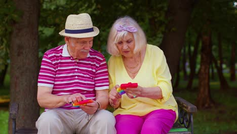 Stylish-senior-grandmother-grandfather-playing-squeezing-anti-stress-toy-simple-dimple-game-in-park