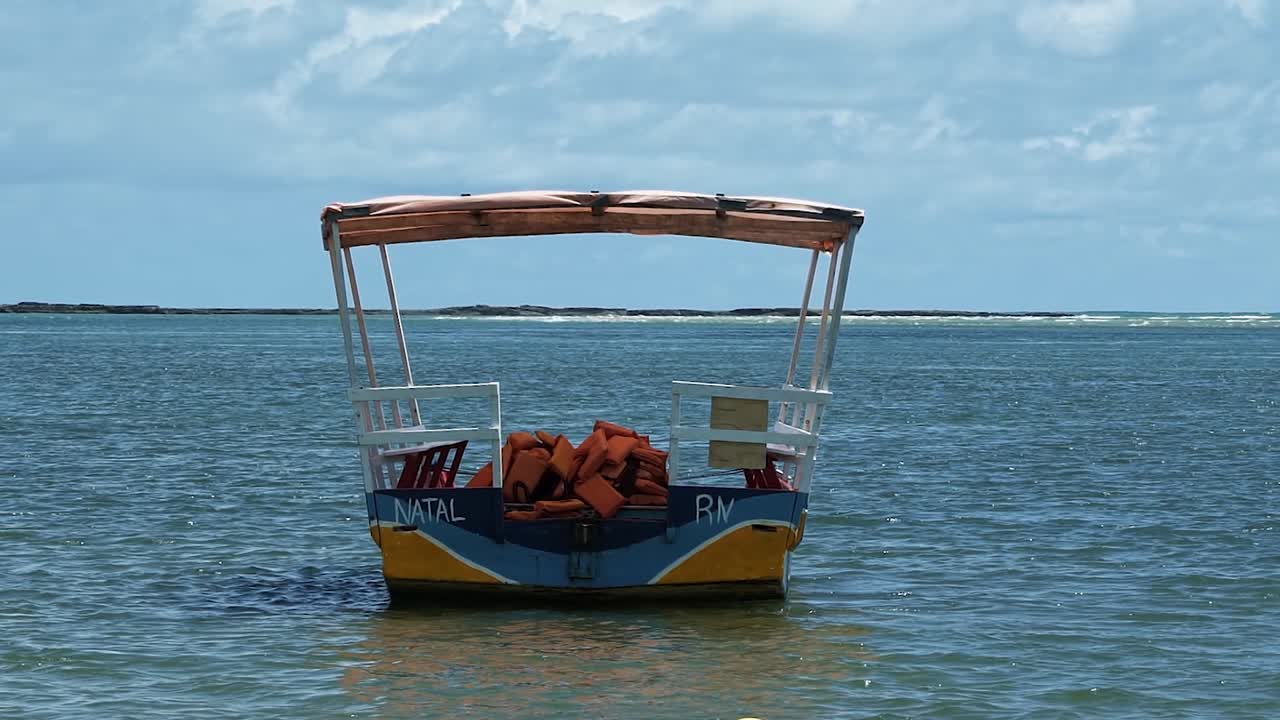 toma en cámara lenta de un pequeño barco de transporte turístico atracado en la orilla de la playa barra de cunhau en la pequeña ciudad costera de canguaretama cerca de natal en el estado de rio grande do norte, brasil