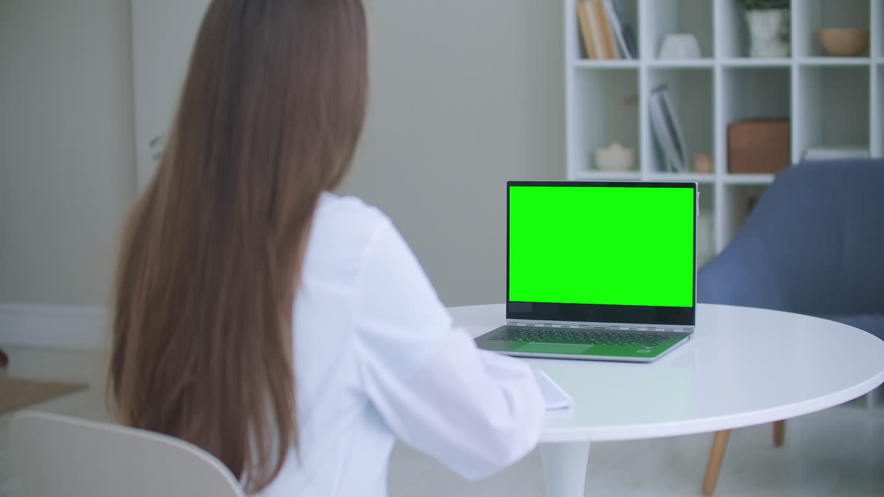 trabajador médico una mujer con una bata blanca utiliza una tableta en la oficina en el escritorio chromakey en la pantalla de la tableta una vista sobre su hombro. médico hablando a la computadora portátil con pantalla verde.