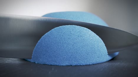 Hemisphere-of-blue-kinetic-sand-is-cut-with-a-large-knife