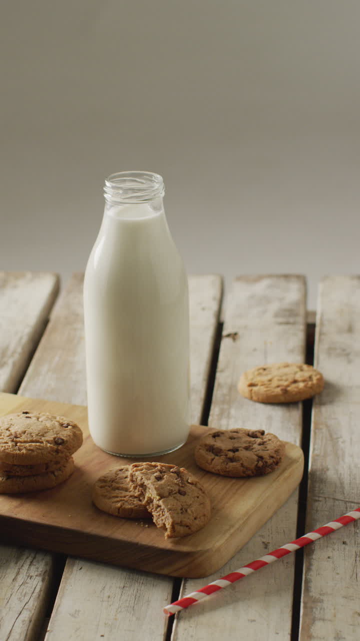 video vertical de galletas de chispas de chocolate y un vaso de leche en la tabla de cortar y fondo de madera