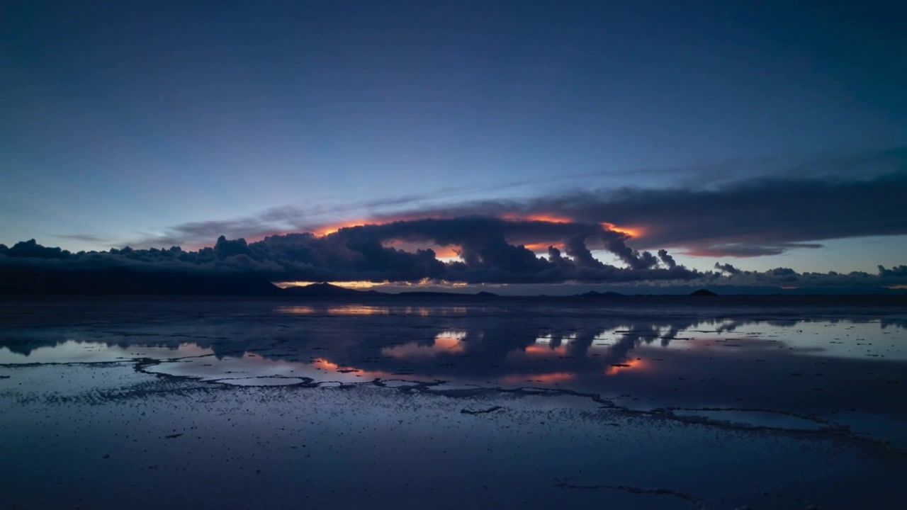 Bevægende lavt skydække reflekteres på en saltslette i skumringen, mens sollyset kaster et orange skær.