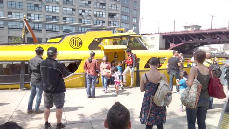 people boarding a bright yellow water taxi at an urban dock