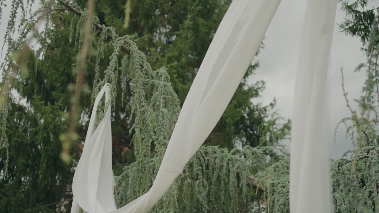 Soft white fabric decoration moving outdoors with trees in background