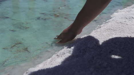 man touches the surface of crystal clear and calm water in the salinas grandes salt pond