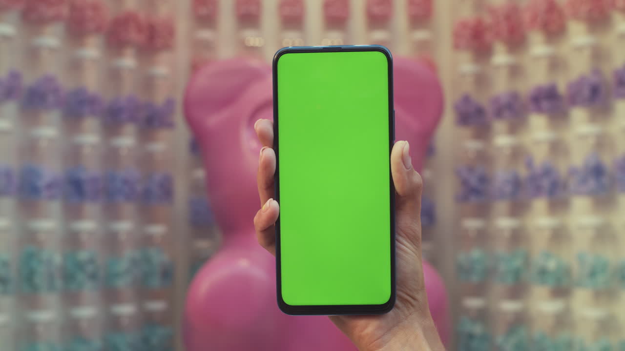 A hand holds a smartphone with a green screen in a retail setting