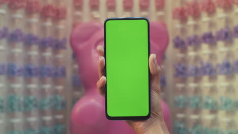 a hand holds a smartphone with a green screen in a retail setting