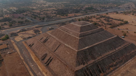 Backwards-reveal-of-ancient-huge-pyramid.-Tilt-up-to-view-dry-landscape.Ancient-site-with-architecturally-significant-Mesoamerican-pyramids,-Teotihuacan,-Mexico