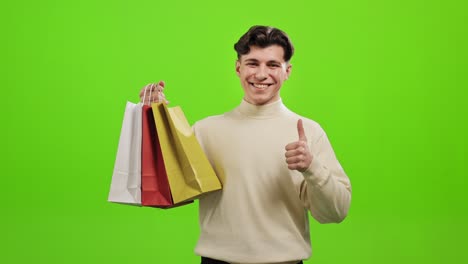 el hombre está de pie y mirando a la cámara. está recogiendo las bolsas de compras y sonriendo. está haciendo un gesto con el dedo hacia arriba. está de pie sobre un fondo verde. pantalla verde. 4k.