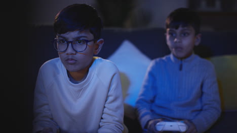 Front-View-Of-Two-Young-Boys-At-Home-Having-Fun-Playing-With-Computer-Games-Console-On-TV-Holding-Controllers-Late-At-Night-3