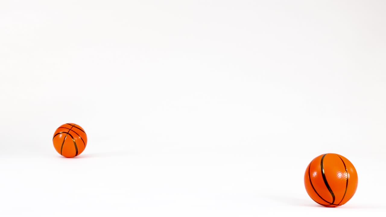 Two small orange basketballs bounce and roll across a clean white studio background