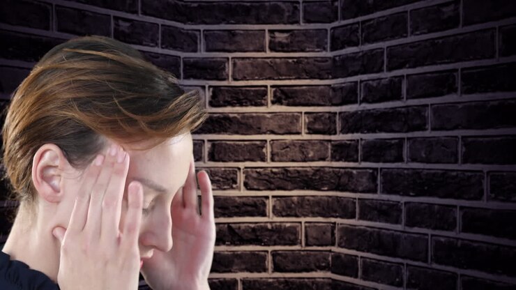 Primo piano di donna caucasica stressata che si tiene la testa, su sfondo con muro di mattoni.