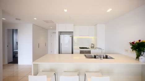 small modern clean white tiled apartment interior kitchen with bar seating and floral flower bouquet