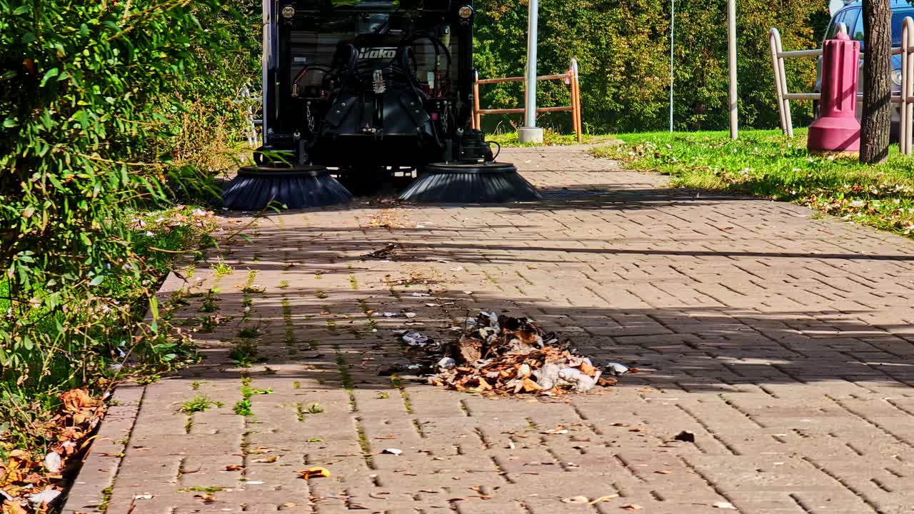 Street cleaner sweeps autumn leaves on Riga pathway, serene scene