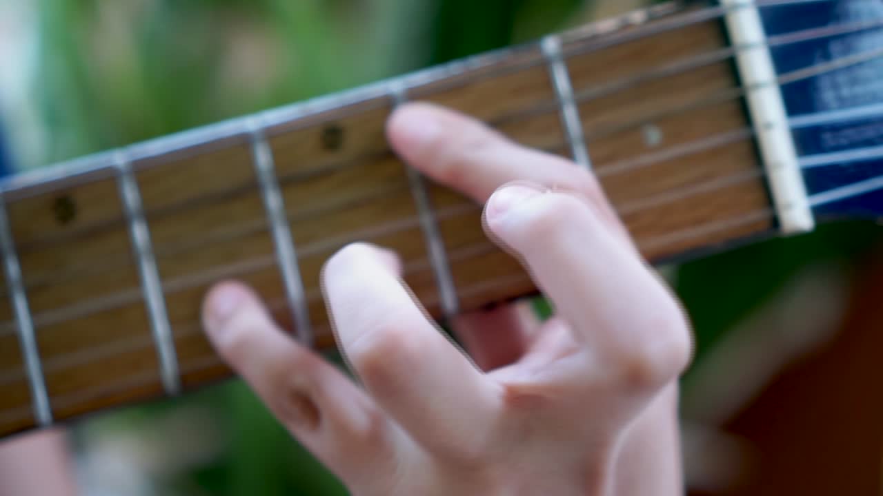 Extreme close up of young boy playing chords on fret board of acoustic guitar