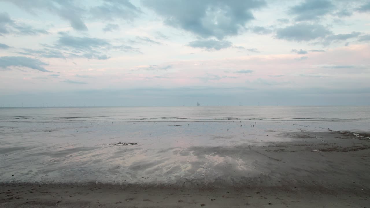 Above, there's aerial footage of a picturesque sunset beach, complete with glistening wet sand, a serene purple and pink sea, and people walking their dog in silhouette
