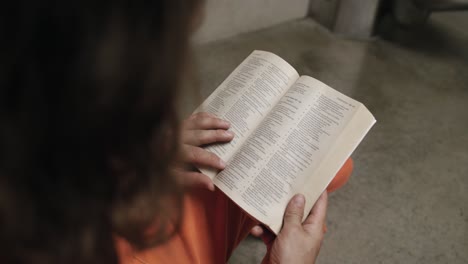 um close de um prisioneiro em sua cela lendo uma bíblia