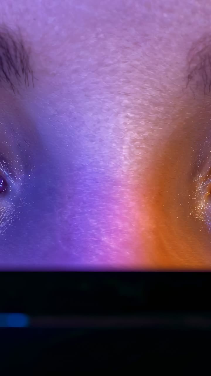 Vertical video: Showing tight face absorbing screen light in dark room, device casting purple glow