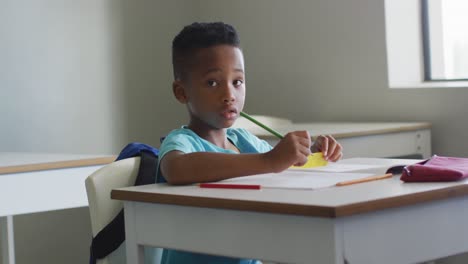 Video-of-african-american-boy-sitting-at-desk-during-lesson-in-classroom