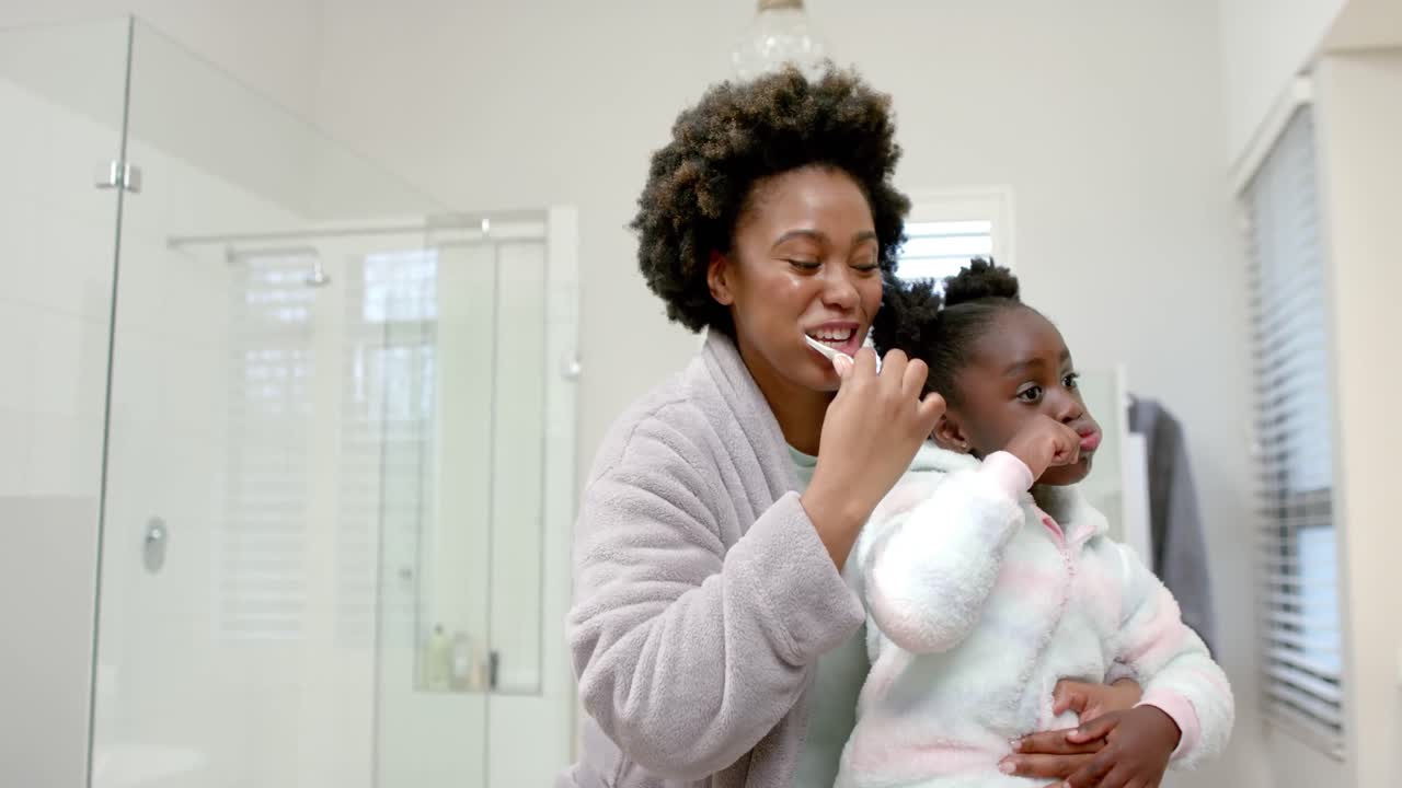 Mãe e filha afro-americanas felizes escovando os dentes no banheiro, em câmera lenta.
