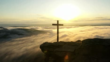 golden sunlight illuminates a wooden cross atop a rocky mountain, rising above a breathtaking sea of clouds