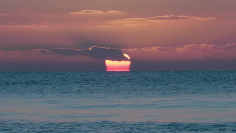 Bird-fly's-across-the-horizon-as-red-sun-sets-over-blue-calm-sea