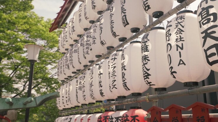 Lanternes japonaises Chochin cylindriques blanches avec du texte Kanji calligraphique noir, suspendues en rangée à l'extérieur. Zoom arrière, plan latéral.