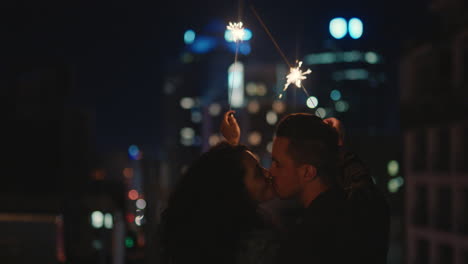 Feliz-Pareja-Caucásica-Besándose-En-La-Azotea-Por-La-Noche-Sosteniendo-Bengalas-Celebrando-El-Aniversario-Disfrutando-De-Una-Romántica-Velada-Urbana