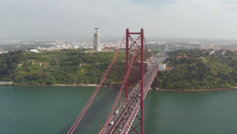 Luftaufnahme-Der-Großen-Roten-Schrägseilbrücke-Vom-25.-April-über-Den-Tejo.-Mehrspurige-Straße-Mit-Starkem-Verkehr-Von-Drohnen.-Statue-Von-Jesus-Auf-Hohem-Sockel.-Lissabon,-Hauptstadt-Von-Portugal.