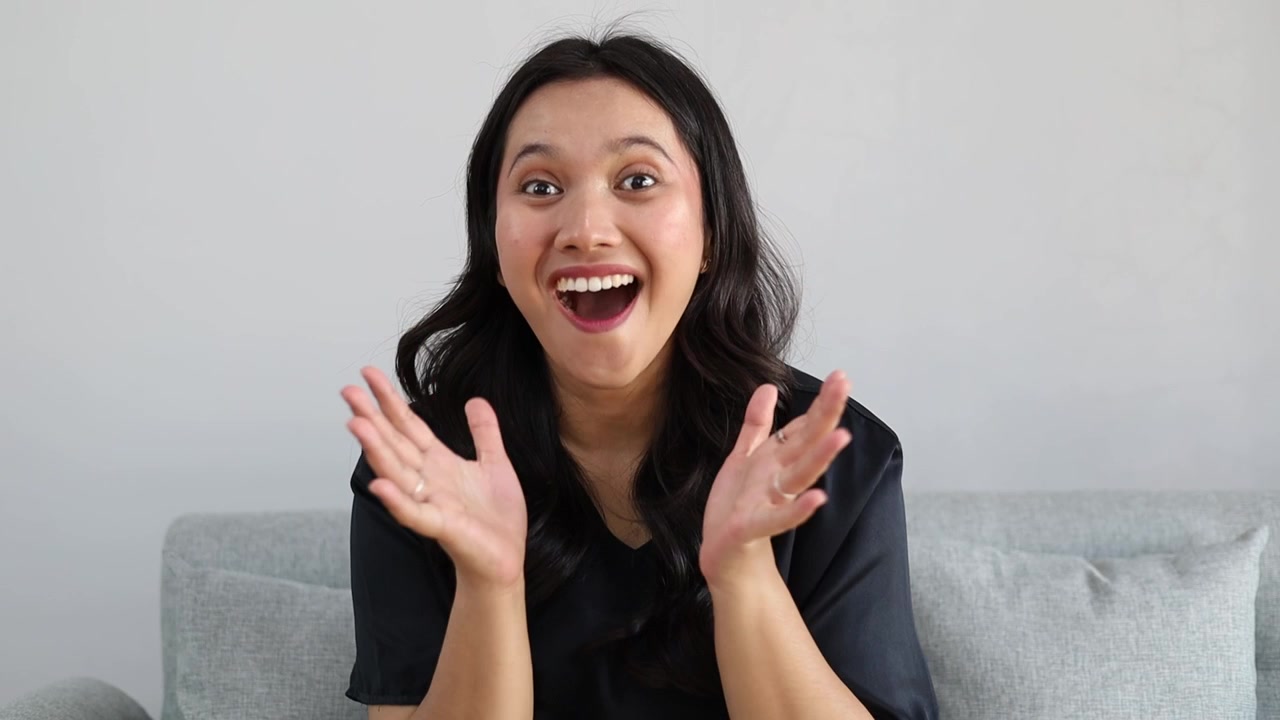 Young attractive Asian woman at home raising eyebrows and opening mouth with surprise after seeing something unexpected
