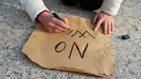 female caucasian hand writes "no war" on a piace of brown paper