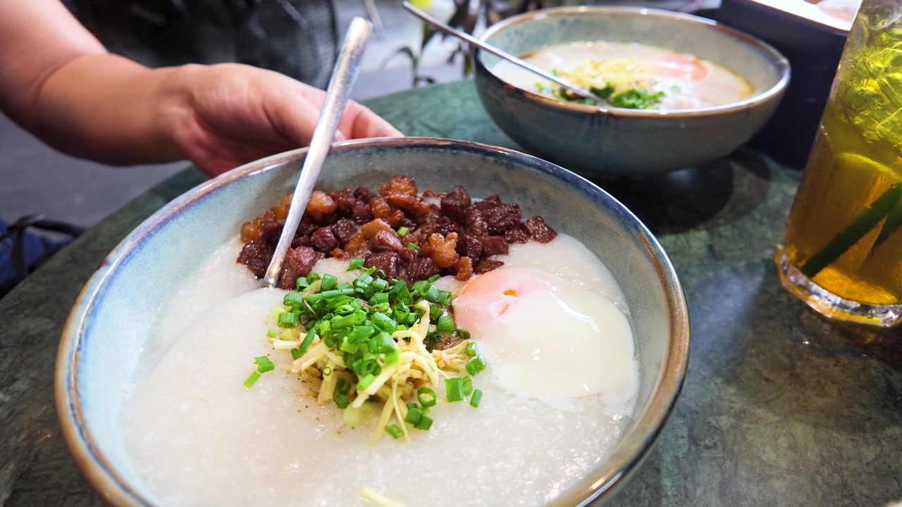 Tampilan dekat sarapan bubur tradisional yang disajikan dengan daging babi cincang, jahe, dan daun bawang.