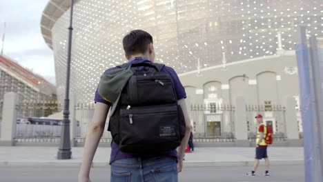 hombre caminando con una mochila delante de un estadio