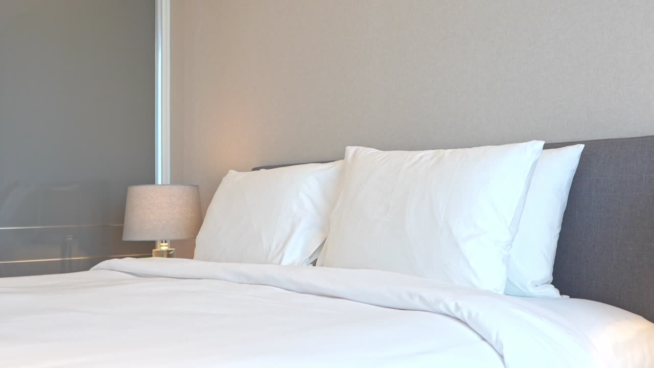 cama tamaño king hecha con funda de lino a rayas blancas y almohadas por la noche con lámparas encendidas en un hotel