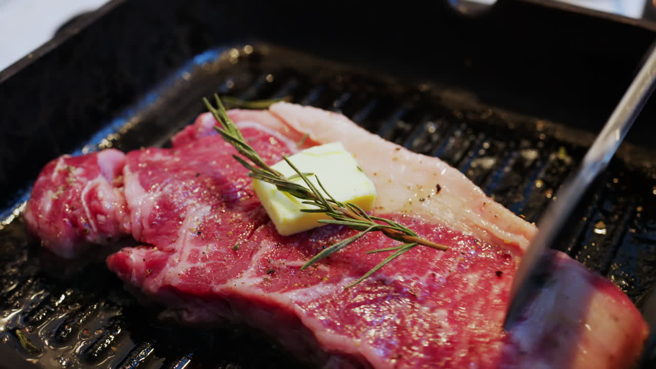 Burro che si scioglie su una bistecca condita che cuoce su una padella griglia calda con rosmarino