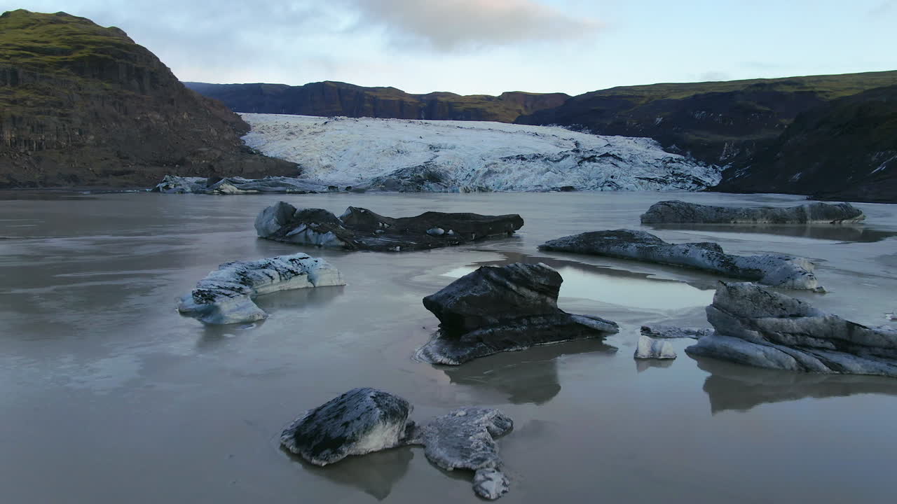 Aerial drone cinematic pan up reveal movement of Solheimajokull glacier Iceland lagoon and icebergs late afternoon
