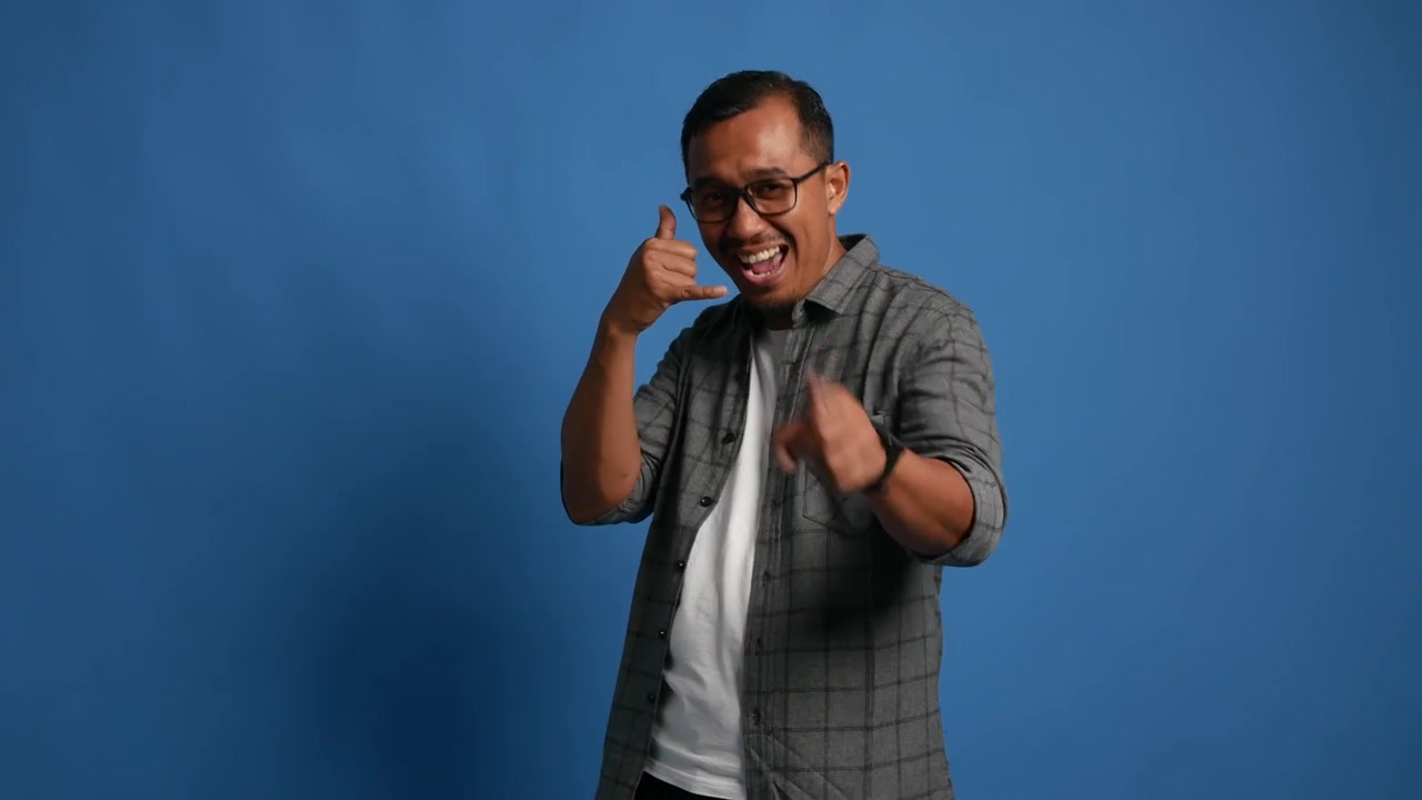 Asian Handsome adult man standing over white background smiling doing phone gesture with hand and fingers like talking on the telephone. Communicating concepts.
