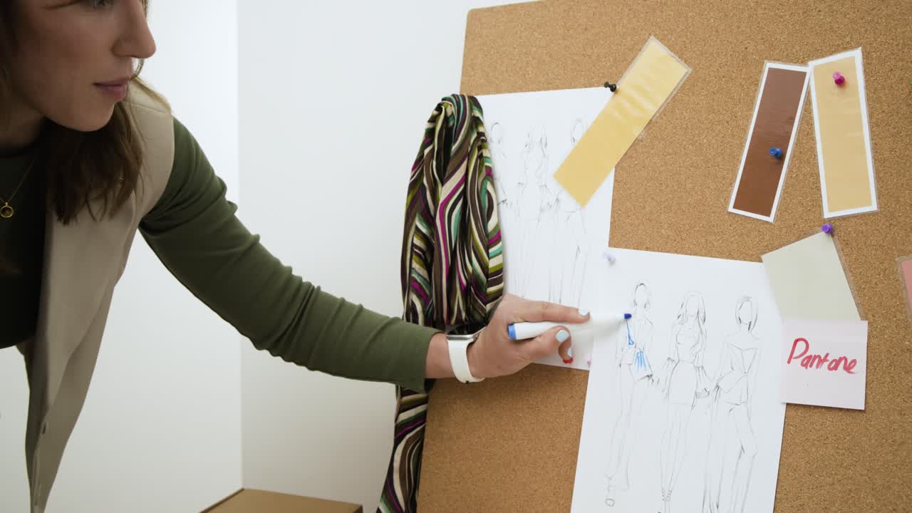 Diverse female coworkers lifting pinned sketch, annotating swatches on corkboard in studio